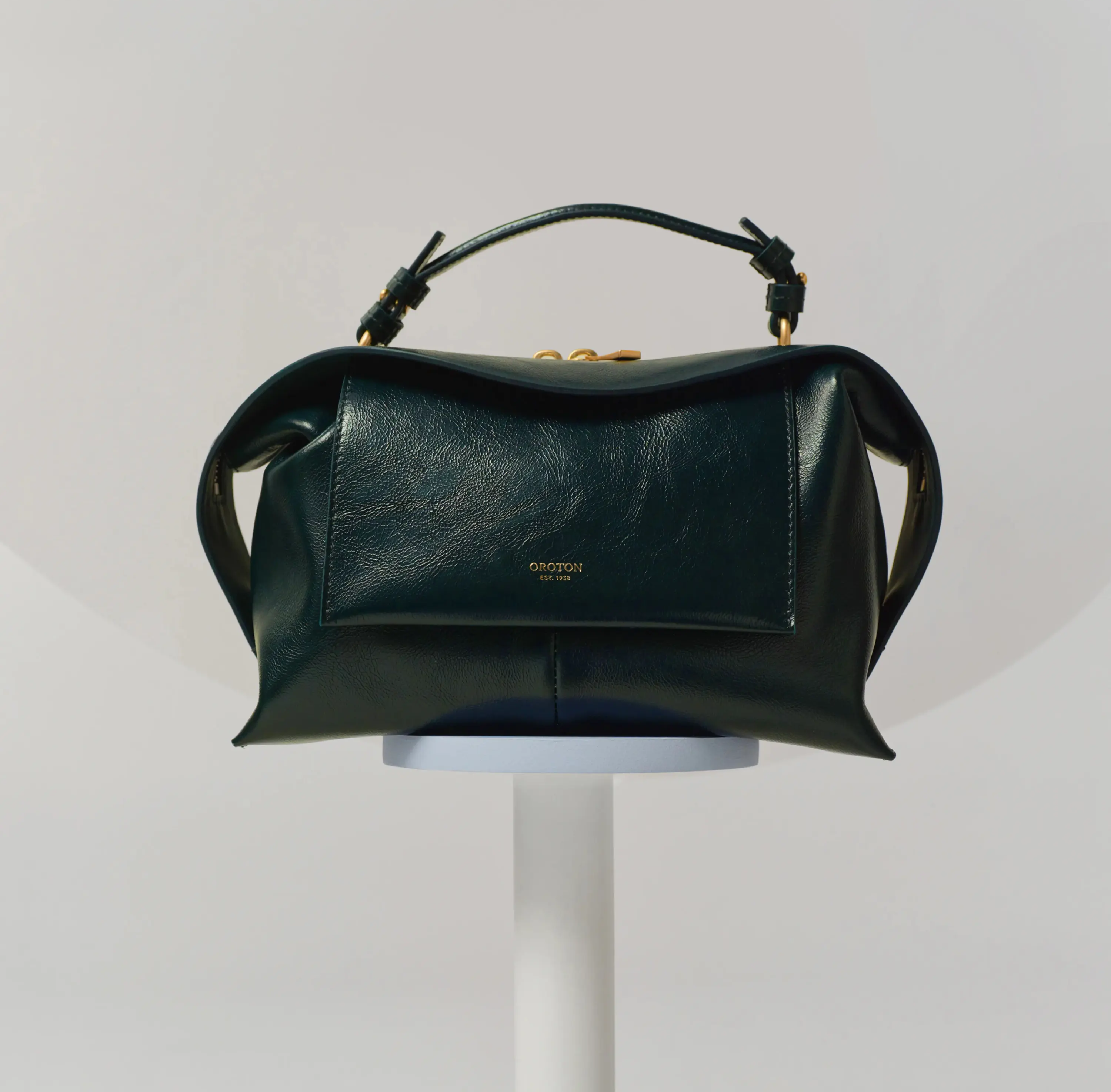 A green leather handbag displayed on a pedestal against a neutral background.