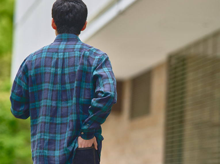 Person walking away, wearing a plaid shirt, in an outdoor setting.