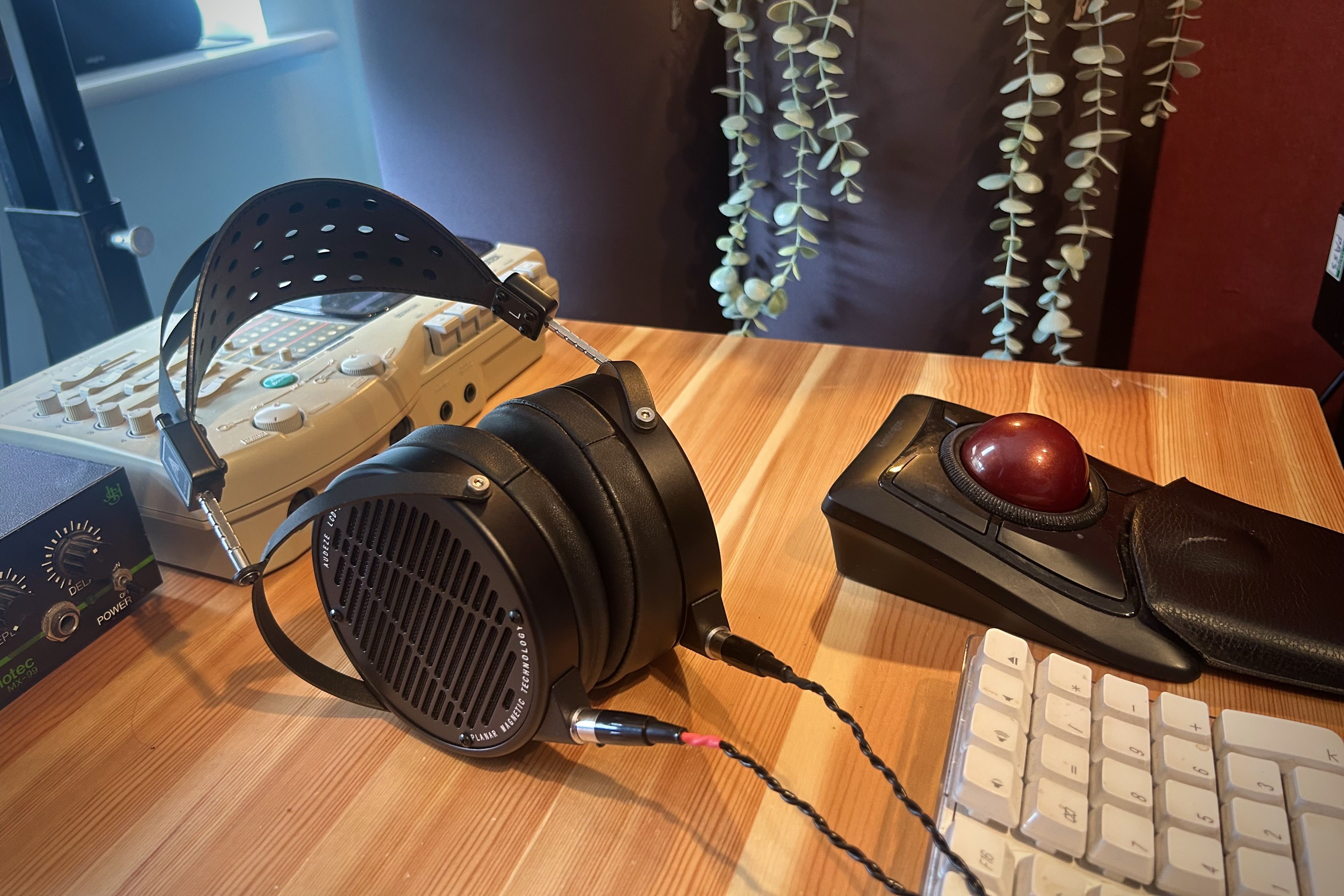 Audeze LCD-X headphones on a wooden desk with a keyboard and a trackball mouse.