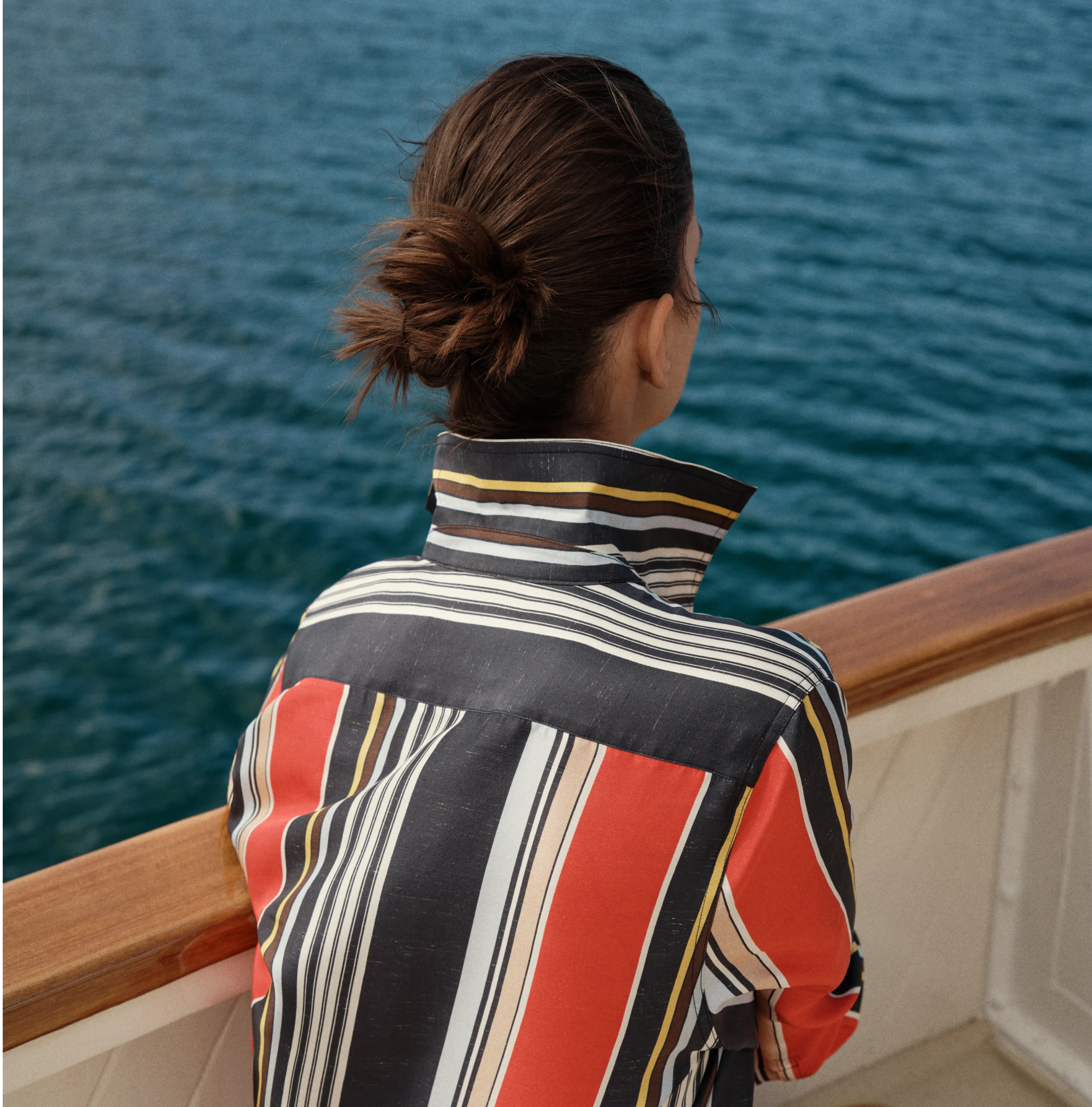 Person in a striped shirt looking at the water from a boat.