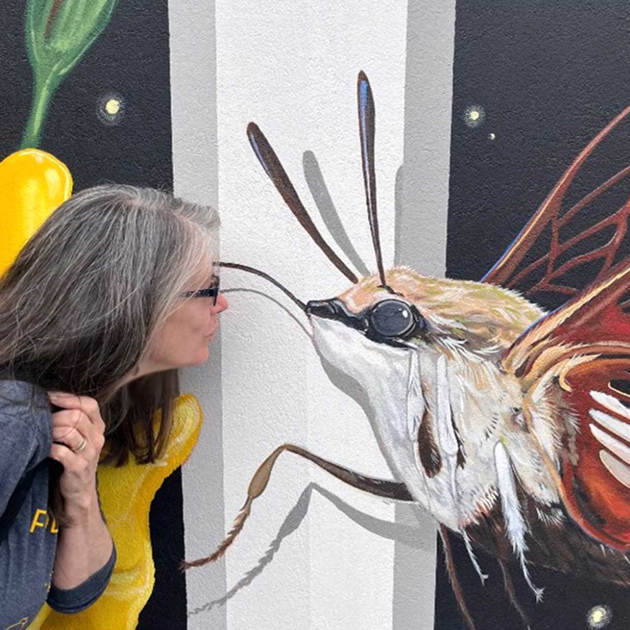 Woman kissing a giant insect mural on a wall.
