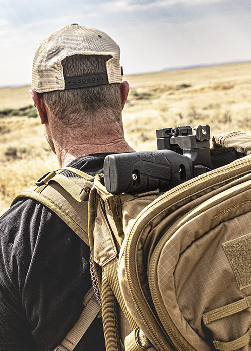 Person wearing a cap and backpack, with a firearm visible.