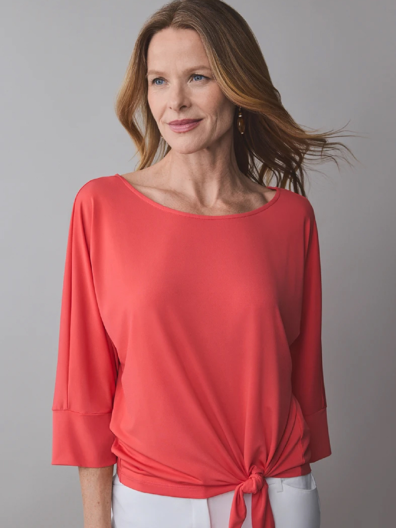 Woman in a coral top with a knot, smiling against a neutral background.