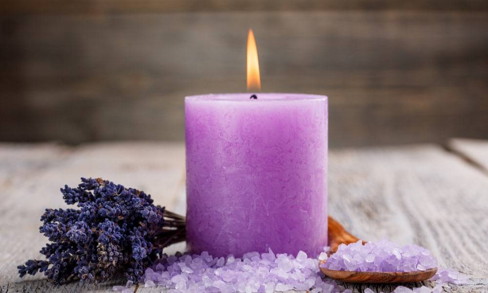 purple candle lit on wood table with salts and lavender sprigs next to it