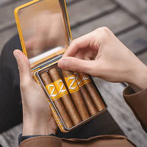 A person holding the opened tin of five Zino Half Corona cigars, taking one cigar out.