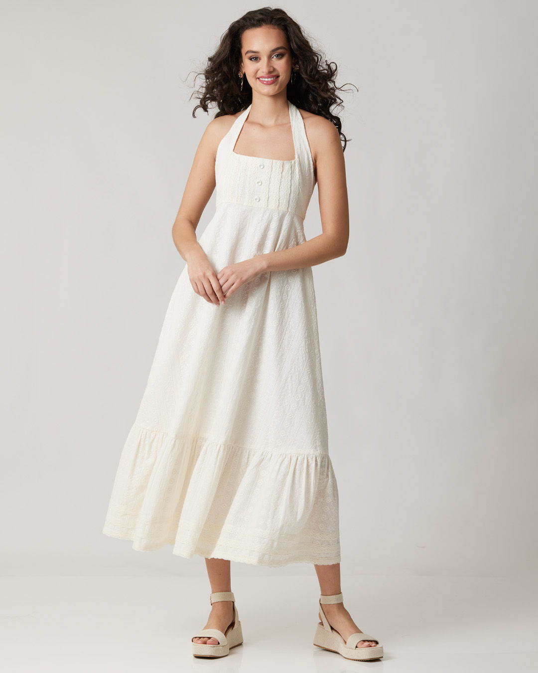 A woman in a white halter dress, standing and smiling.