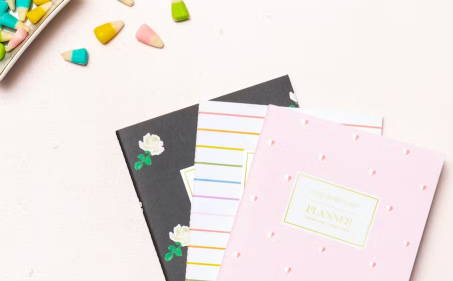 Three of The Home Edit's notebooks on a beige background with candy at top left.
