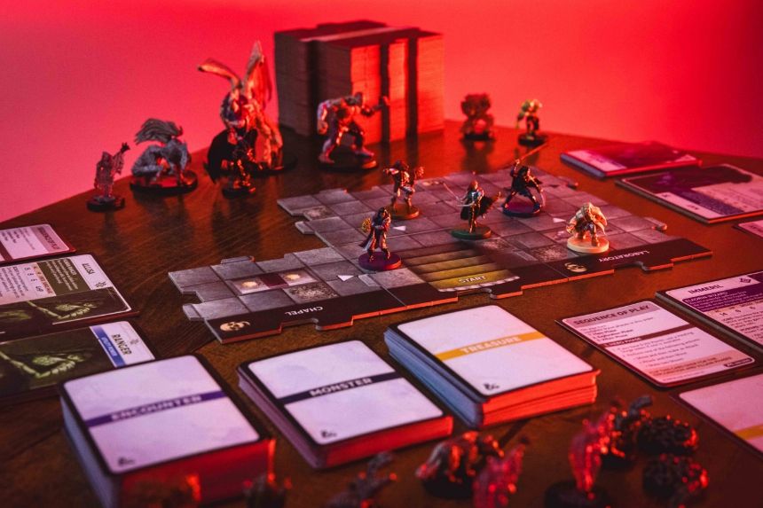 Board game setup with miniatures and cards on a table, under red lighting.