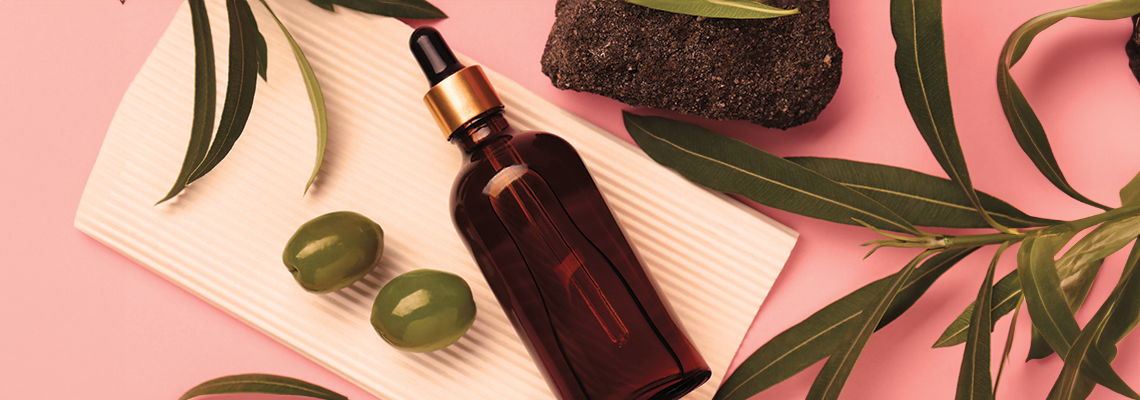 Brown glass dropper bottle with green olives and leaves on a pink background.