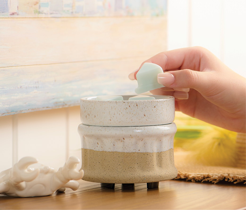 A hand holding a small item above a layered decorative jar.