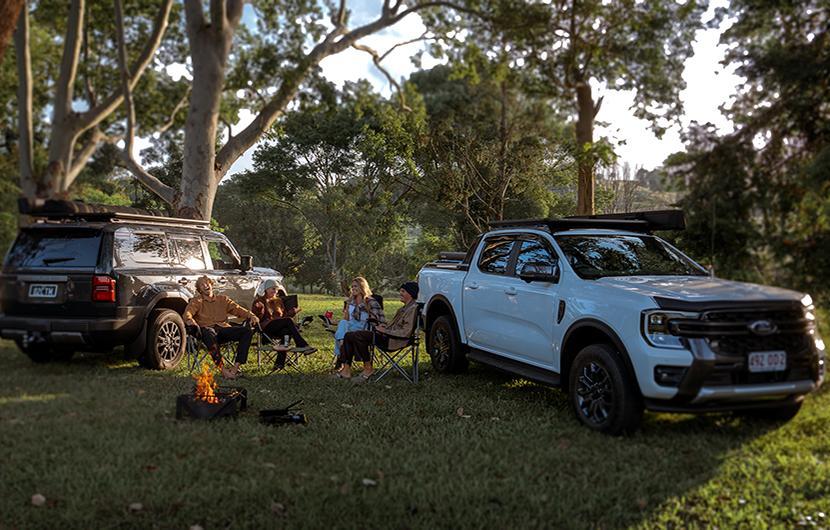 People camping around a campfire with two vehicles outside