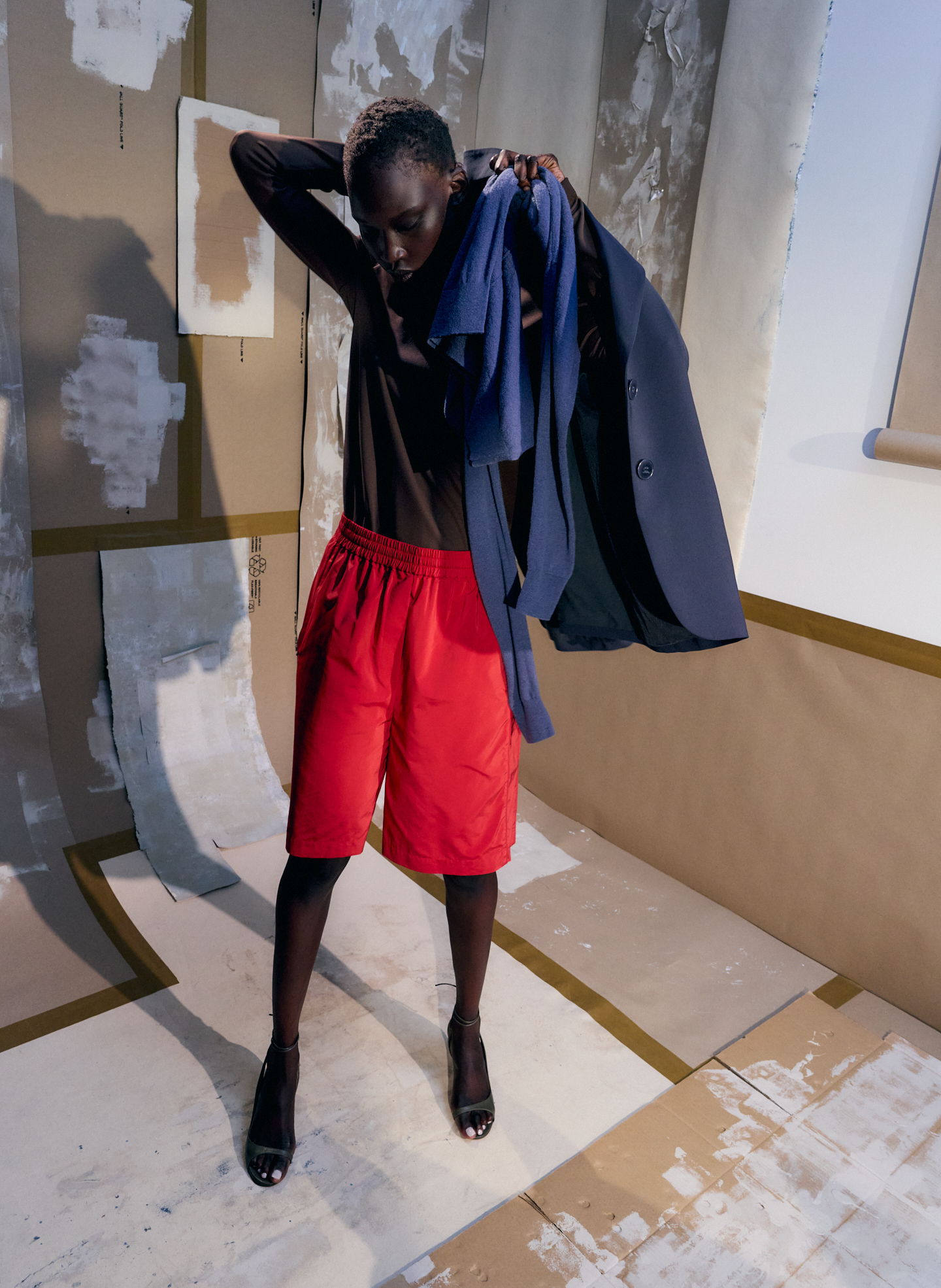 Model wearing red shorts and black top, holding a blue garment.