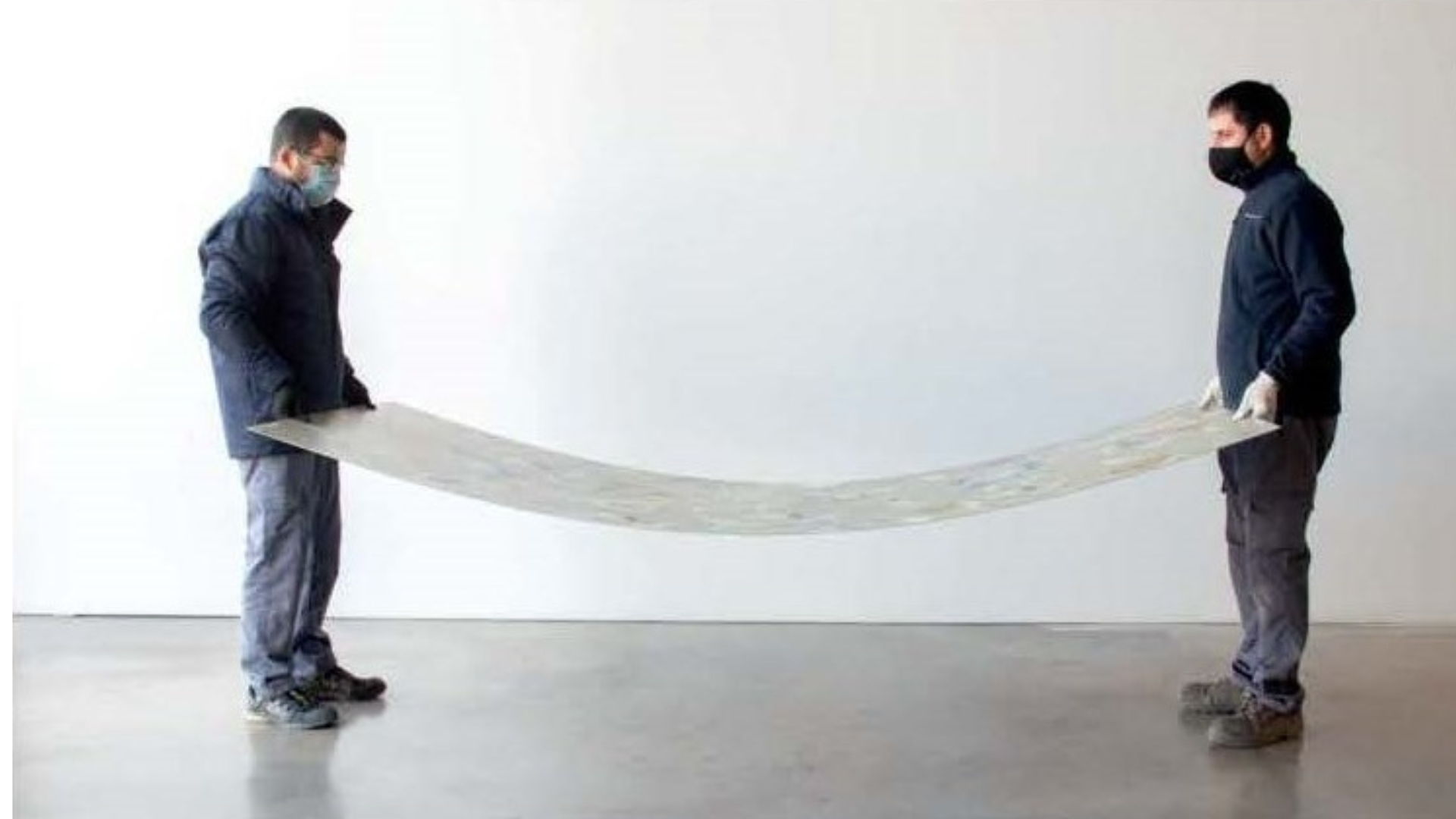 Two individuals holding a long, flexible Alluslate panel between them.