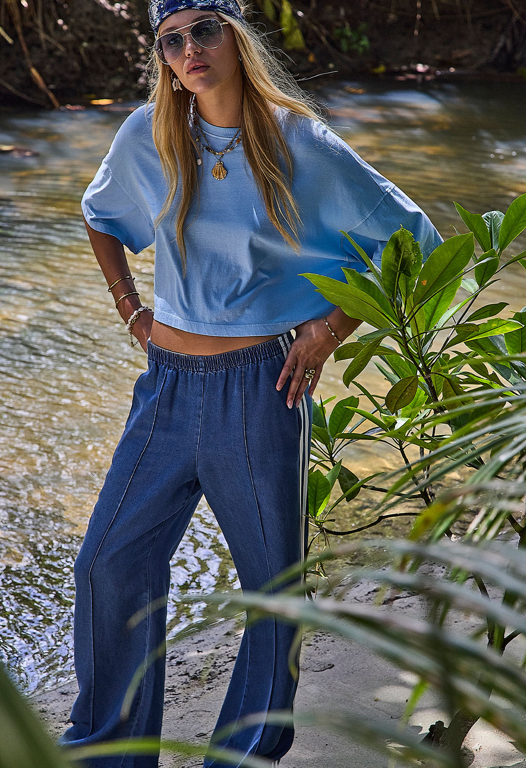 Person in casual outfit standing by a river surrounded by greenery.