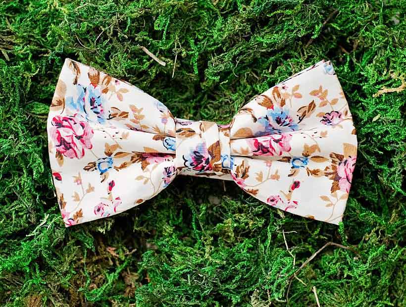 A tan, brown, pink and blue bow tie on a mossy background