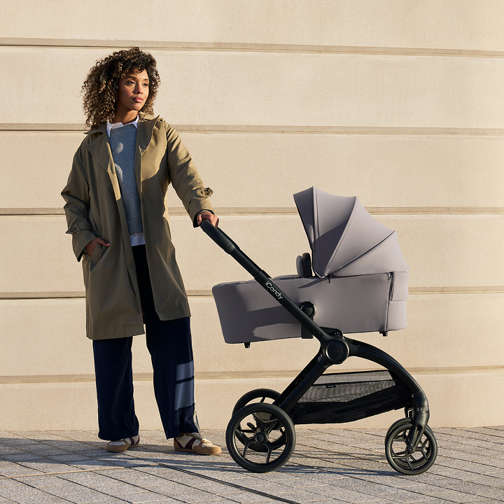 Woman standing with a stroller against a light-colored wall.
