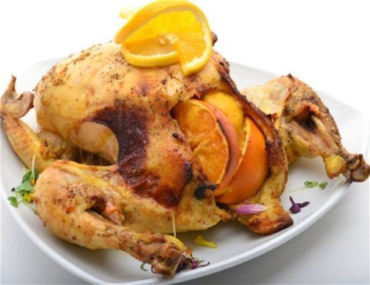 Roasted chicken garnished with orange slices on a white plate.