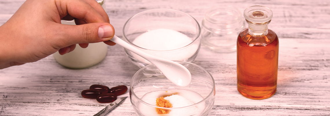 Hand holding a spoon over bowls with sugar and liquid in a bottle.
