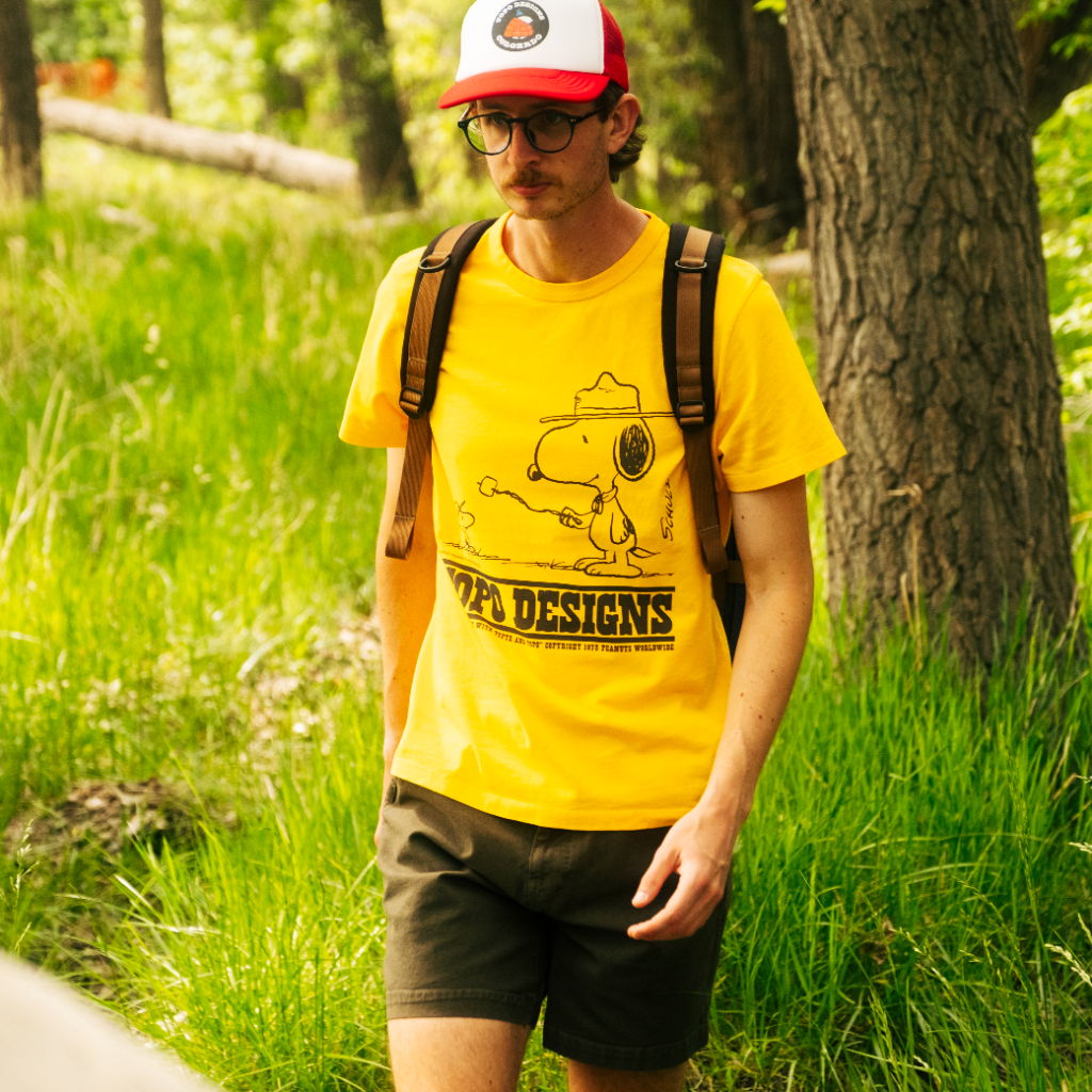 Person walking in a yellow shirt and cap through a forested area.