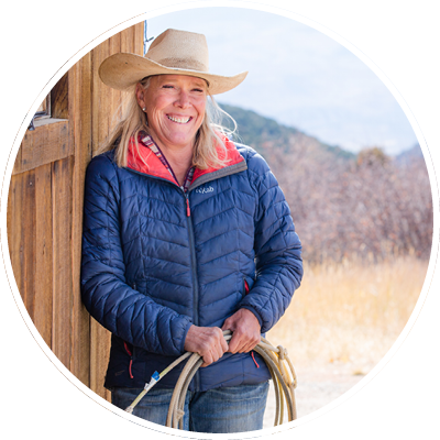 Rancher Julie Hansmire leaning against a barn holding a rope