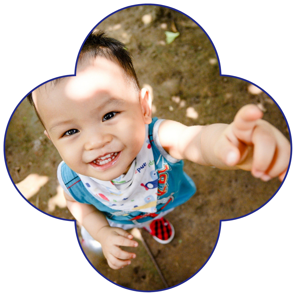 Smiling toddler reaching out with a playful expression outdoors.