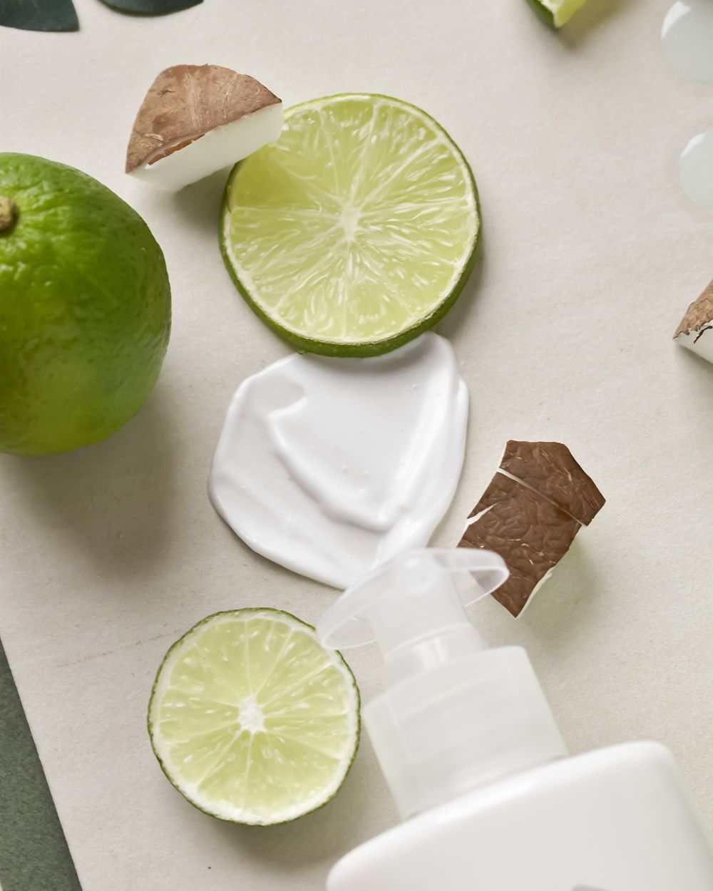 Lime slices and coconut pieces next to a bottle of lotion.