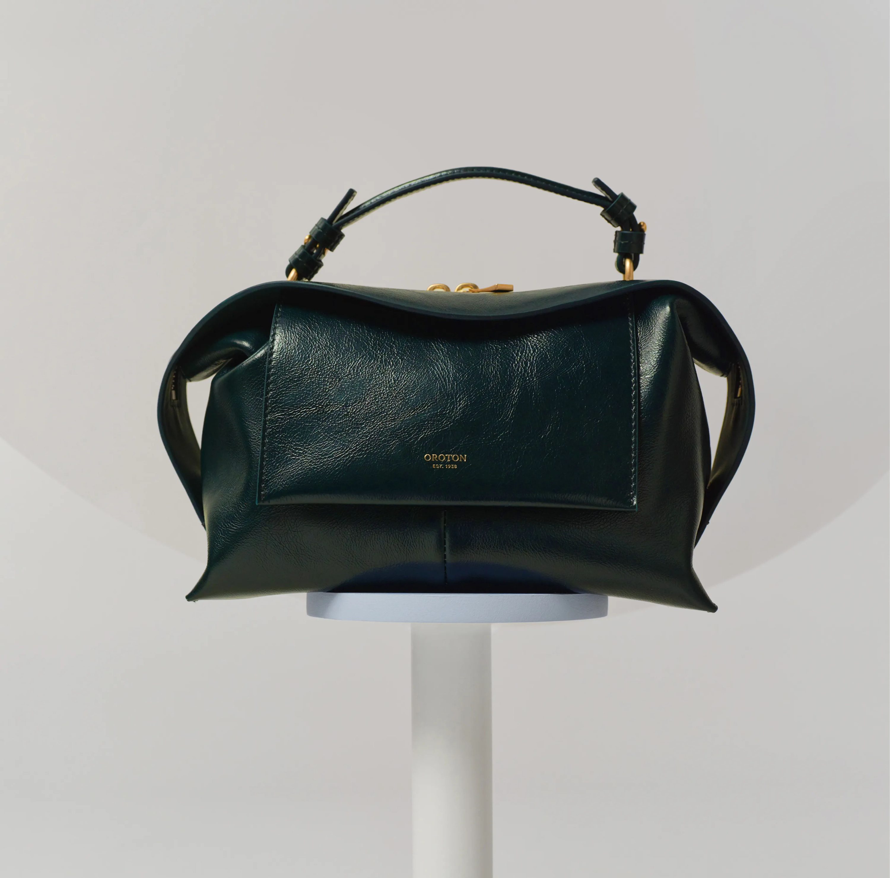A green leather handbag displayed on a pedestal against a neutral background.