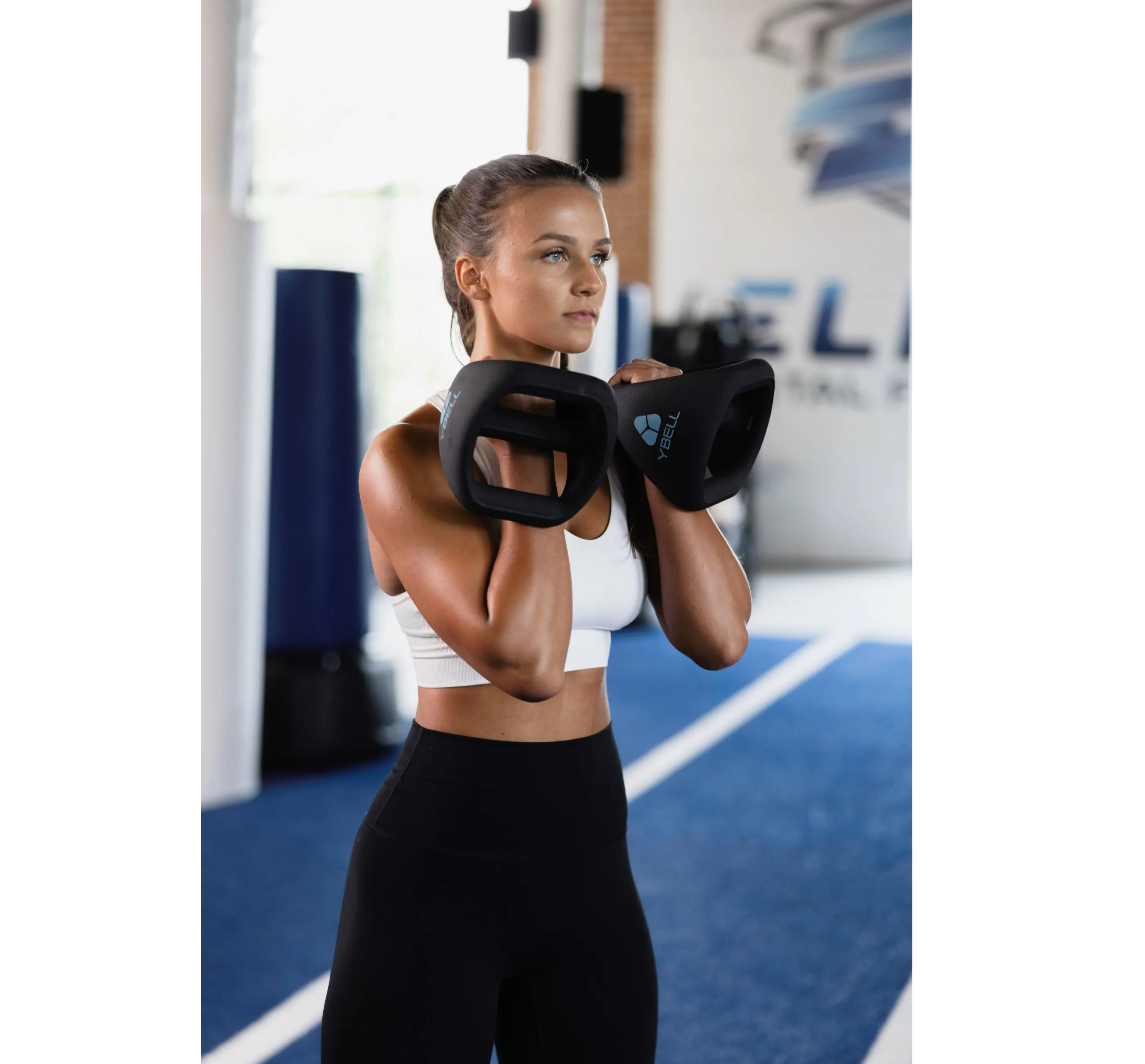 A female athlete hlding YBells using a rack grip inside a fitness studio.