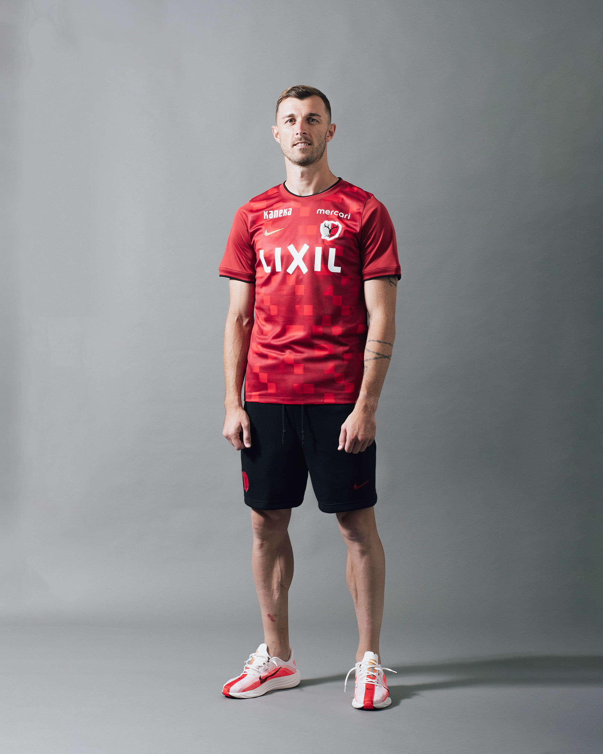 A person wearing a red sports jersey and black shorts, standing against a gray background.