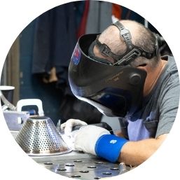 Person wearing a welding helmet, working on metal equipment.