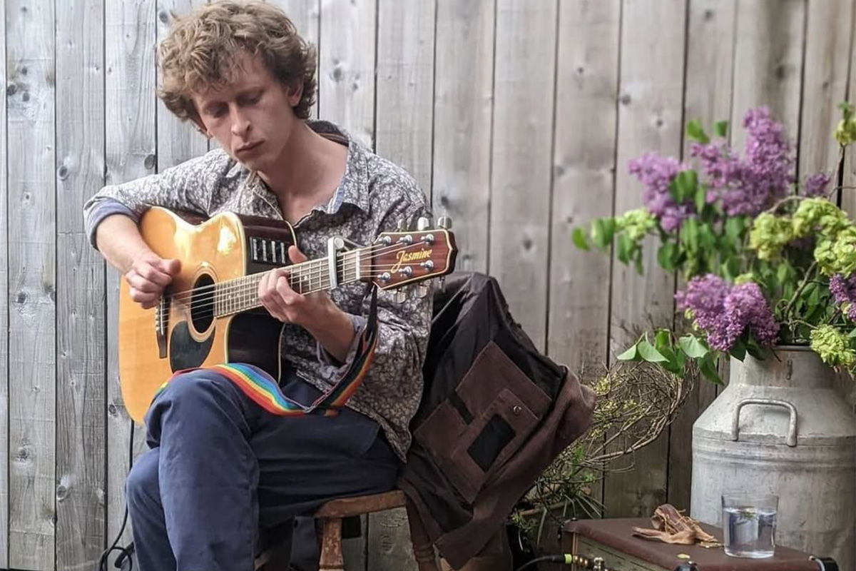 Person playing guitar next to flowers and a wooden fence.