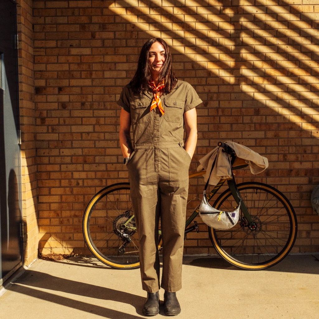 Person in a jumpsuit standing next to a bicycle against a brick wall.