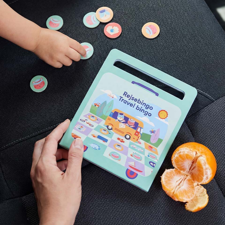 Child's hand playing with tokens next to an educational game and orange.