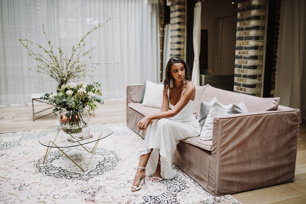 Die Braut trägt ein Seidenkleid auf dem gemütlichen Sofa im Brautladen Grace Loves Lace in Shoreditch