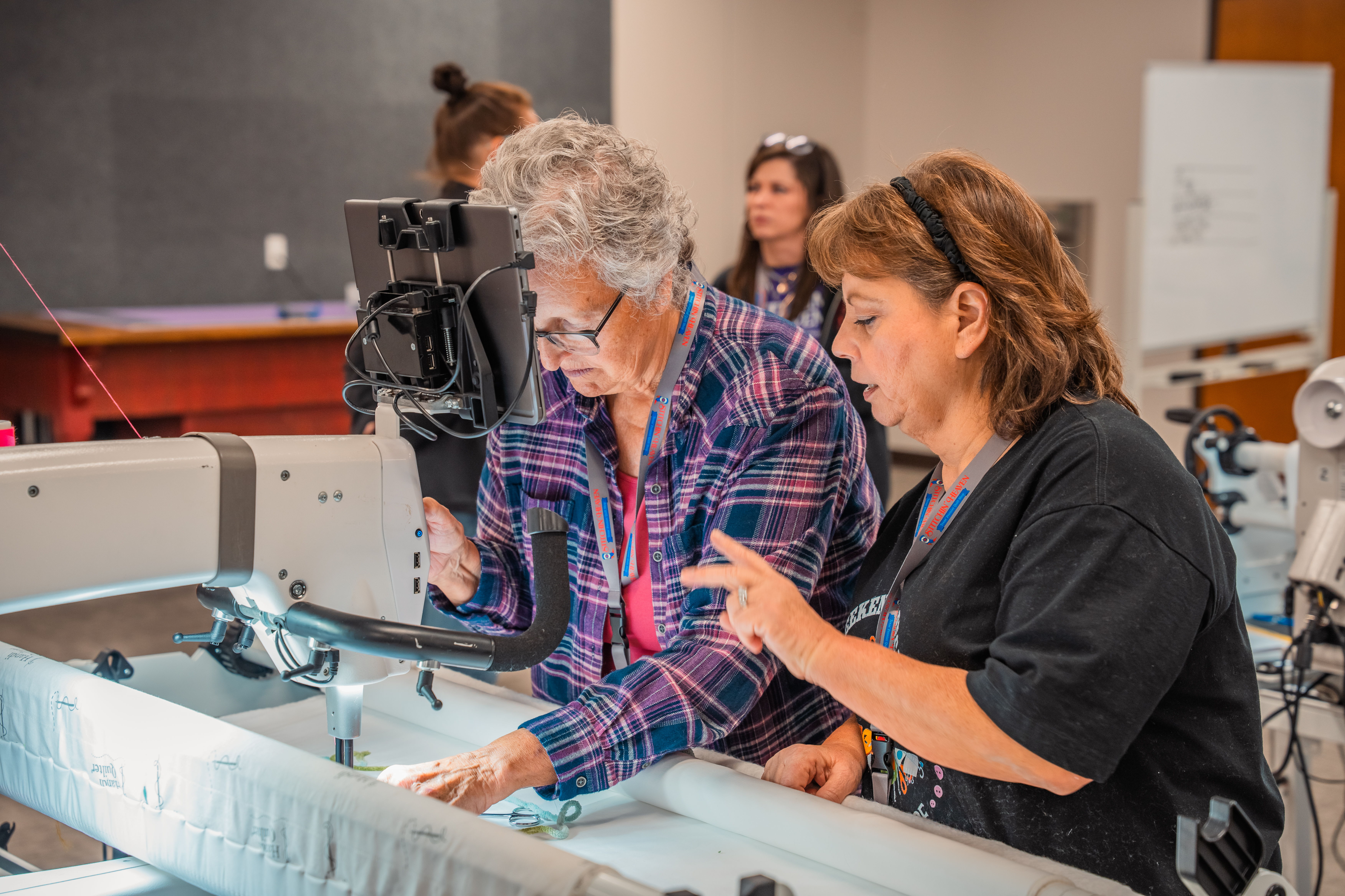 Two women collaborating on a sewing machine in a classroom setting.