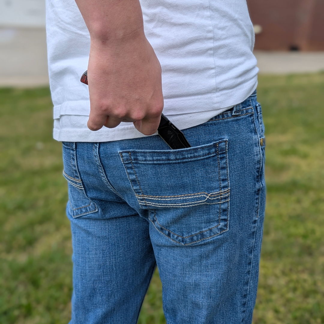 Person holding a knife behind their back while wearing jeans and a white shirt.
