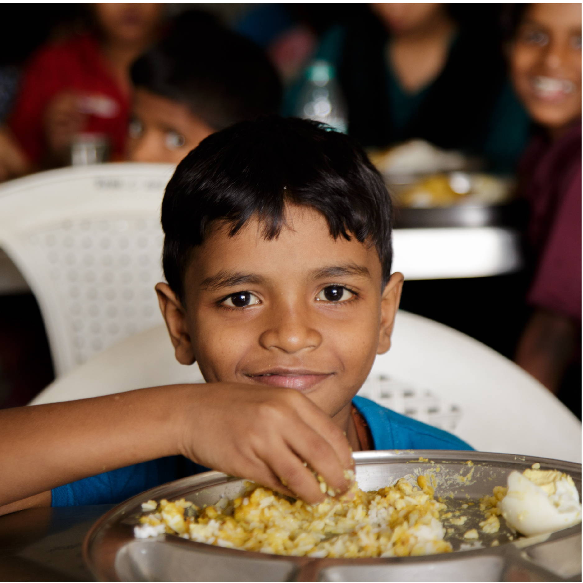 A young Indian boy sits at a table eating some rice and a hard boiled egg. 
