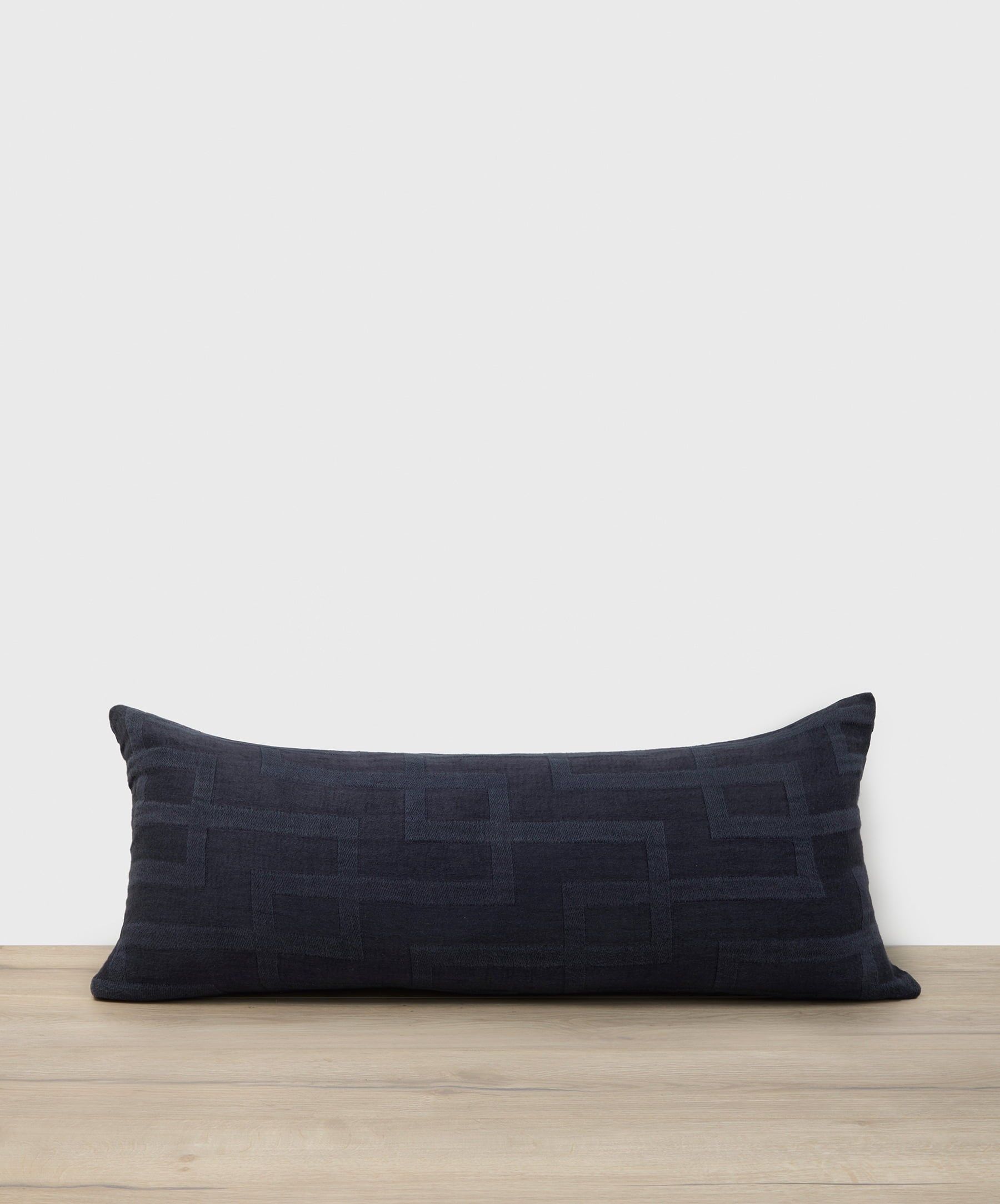 Navy blue pillow with geometric pattern on a wooden surface and light gray background