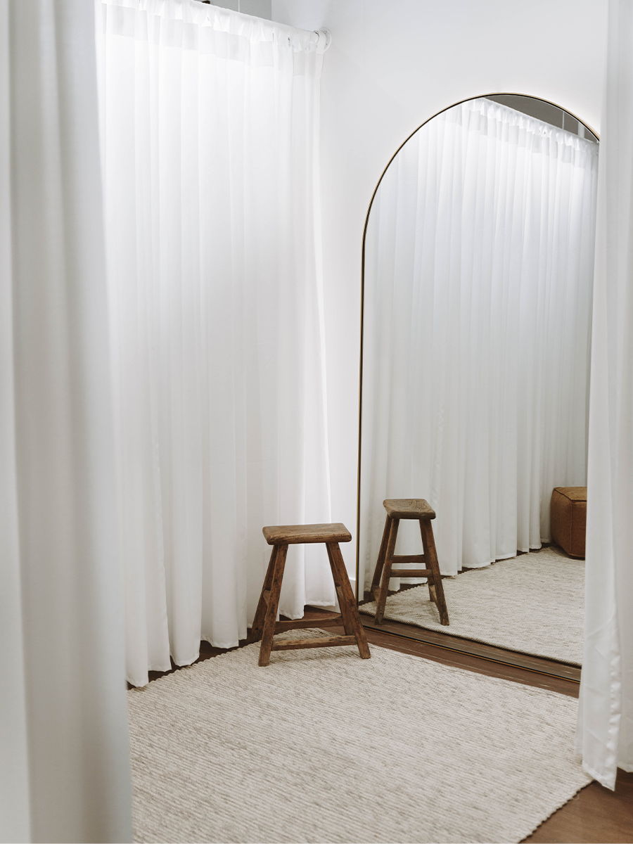 A minimalistic room with a mirror, stool, and white curtains.