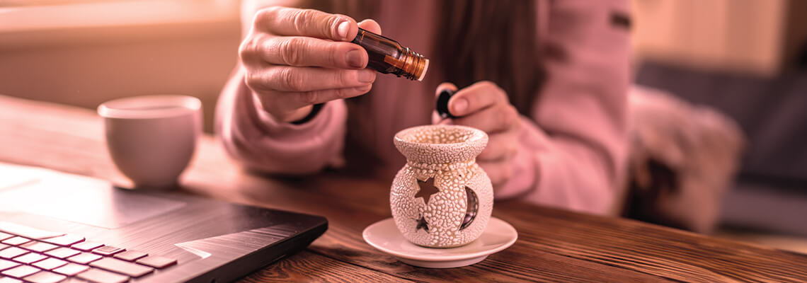 Person adding liquid to a ceramic oil diffuser on a wooden table.