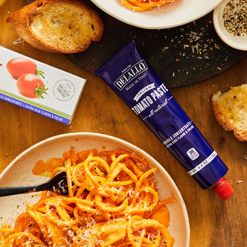 DeLallo Tomato Paste Tube laying next to a bowl of pasta with red sauce