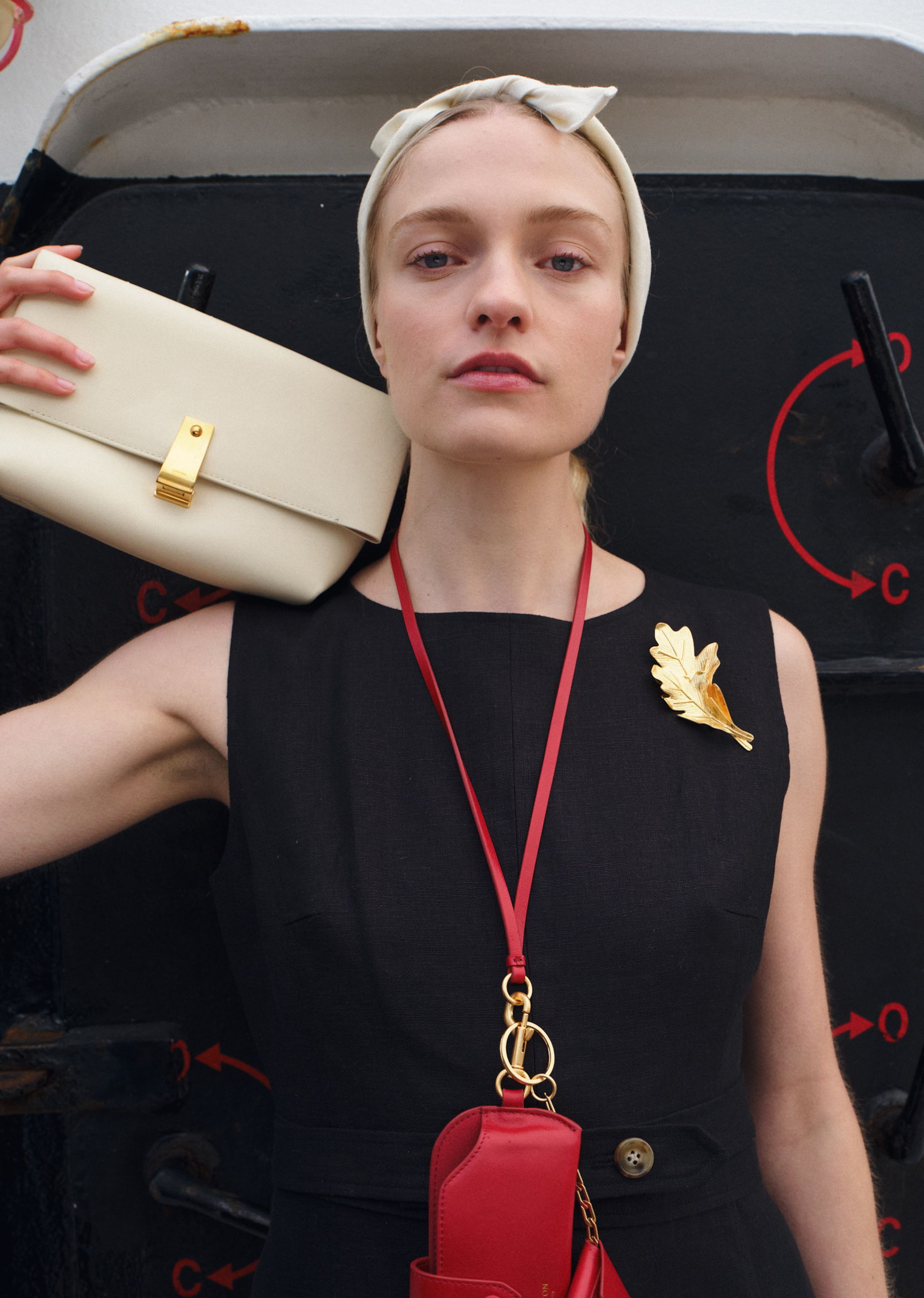 Model holding a clutch bag, wearing a black dress and headscarf.
