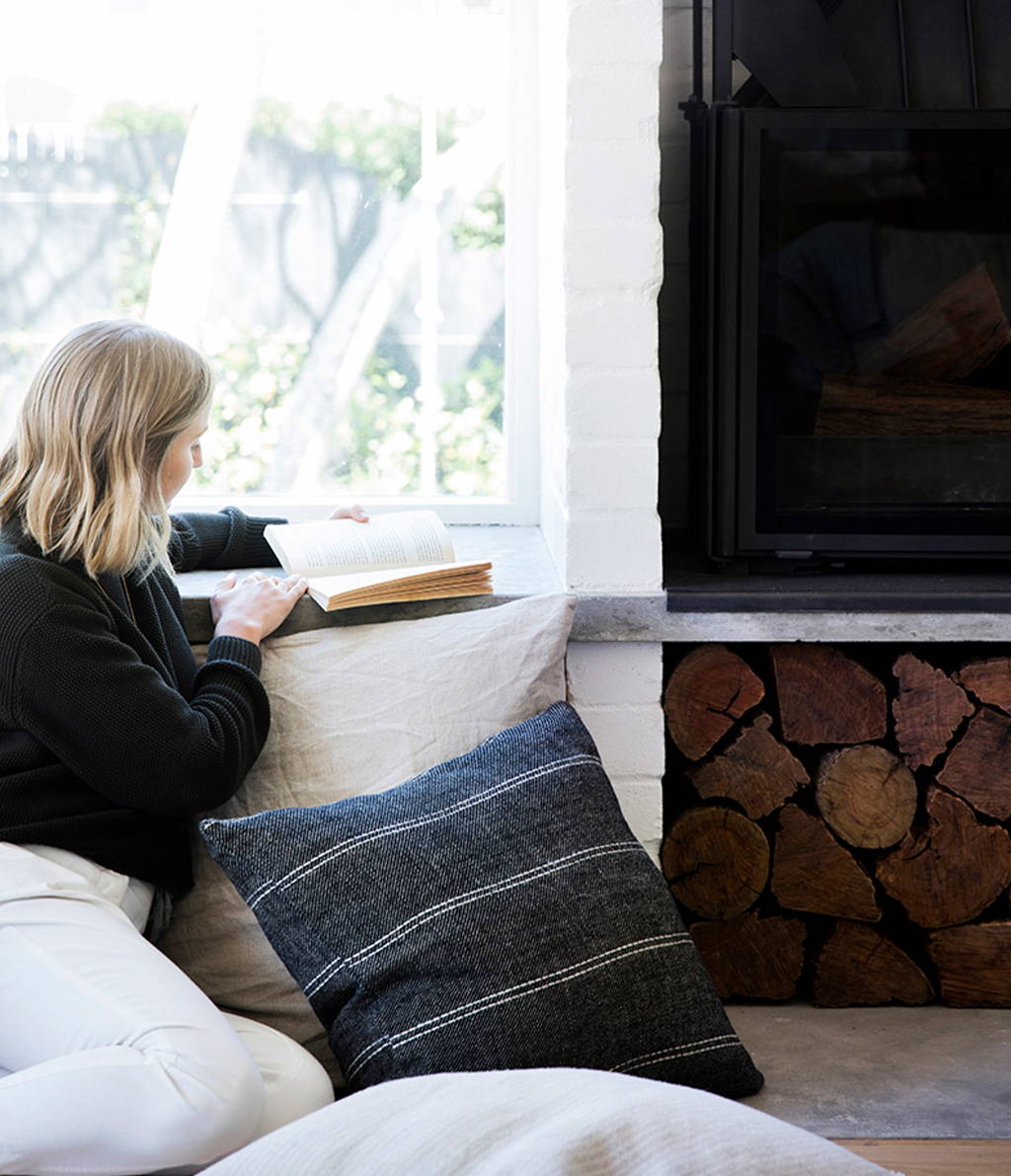 Model reads a book while leaning against Cultiver Euro Pillowcases in Mira Rafa and Natural colours