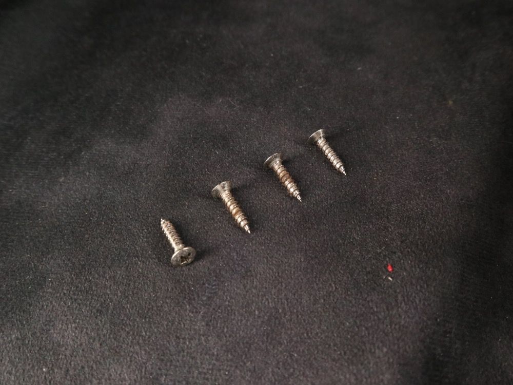 Four metal screws arranged in a row on a dark surface.