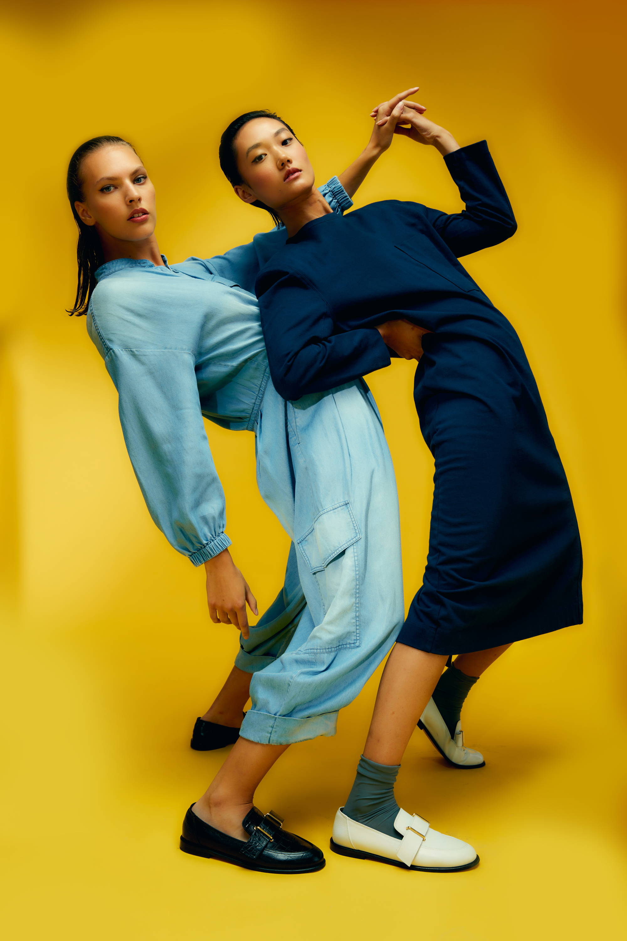 Two models in stylish outfits posing against a yellow background.