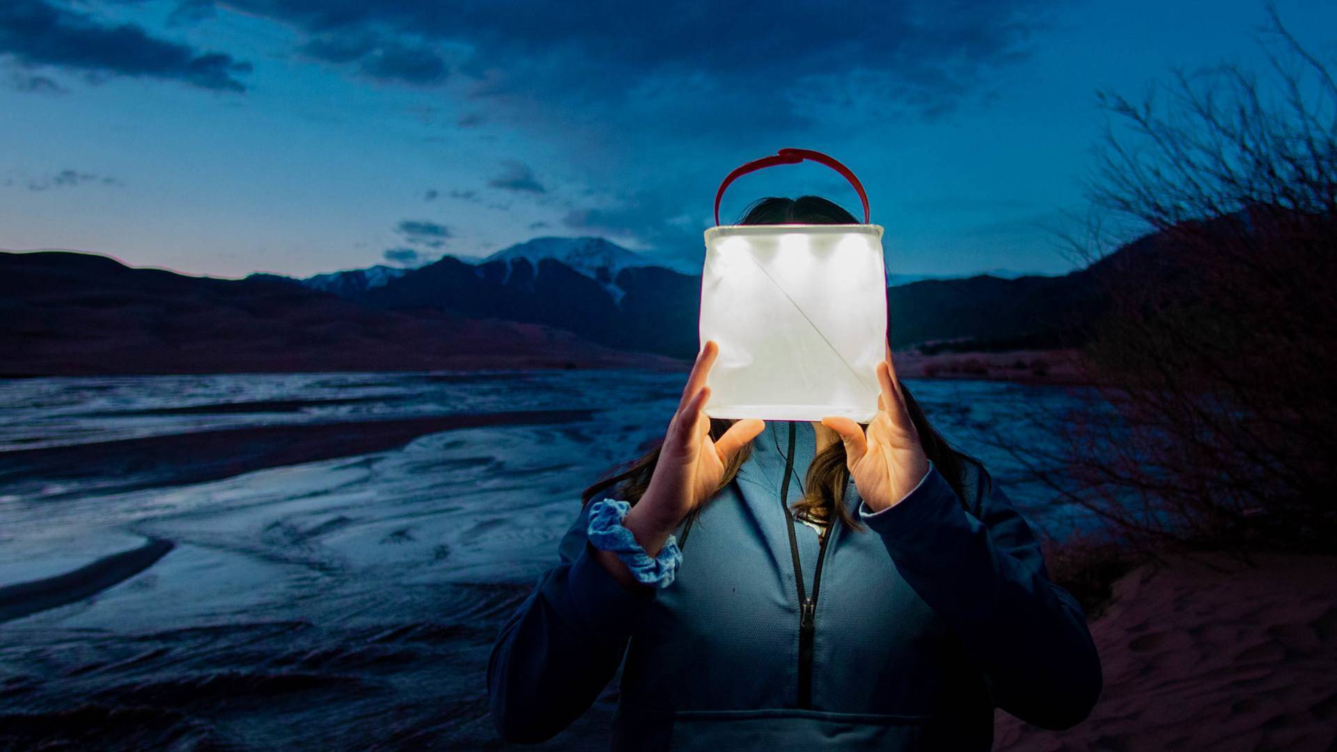 Woman holding lit up lantern infront of her face.