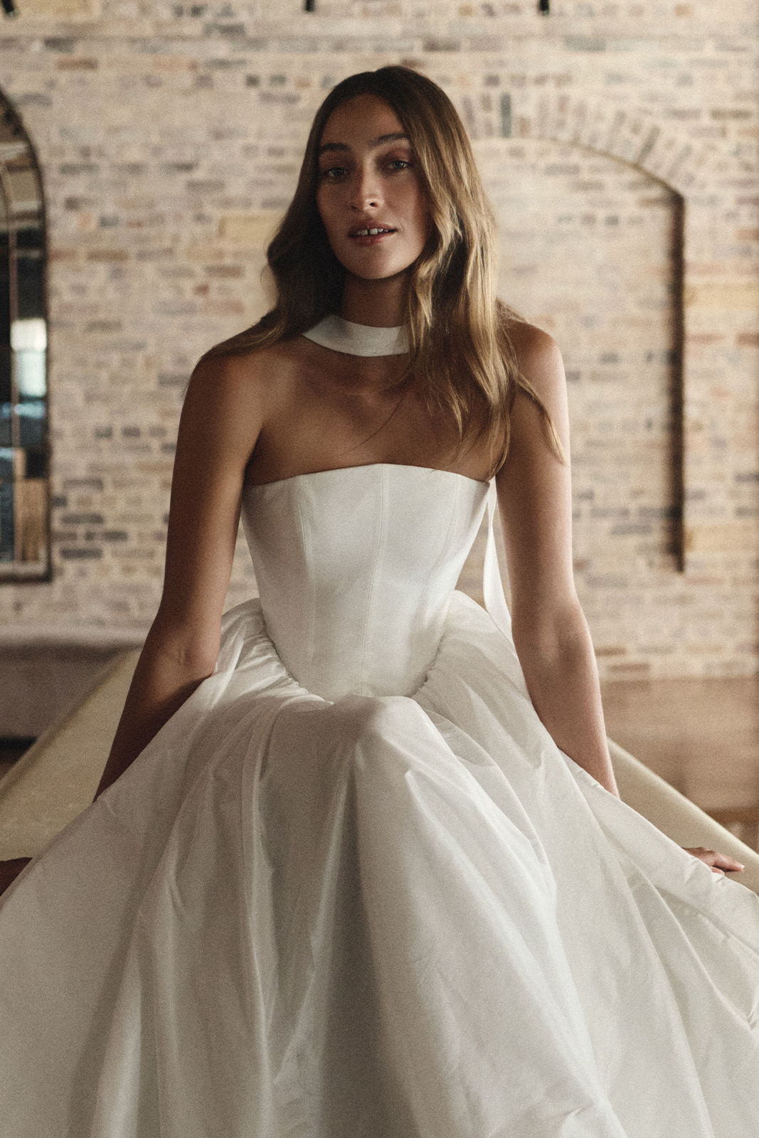 Model wearing a strapless white gown in a rustic setting.