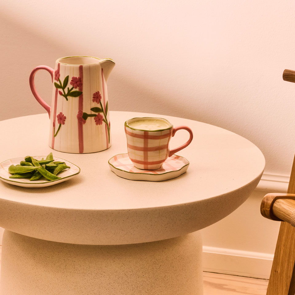 A floral teapot and cup on a round table with a plate of green snacks.