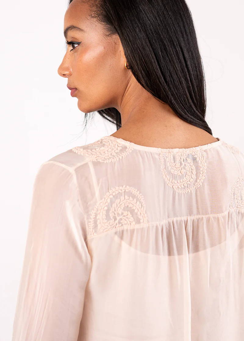 A model wearing a semi sheer blush pink blouse over a white top,