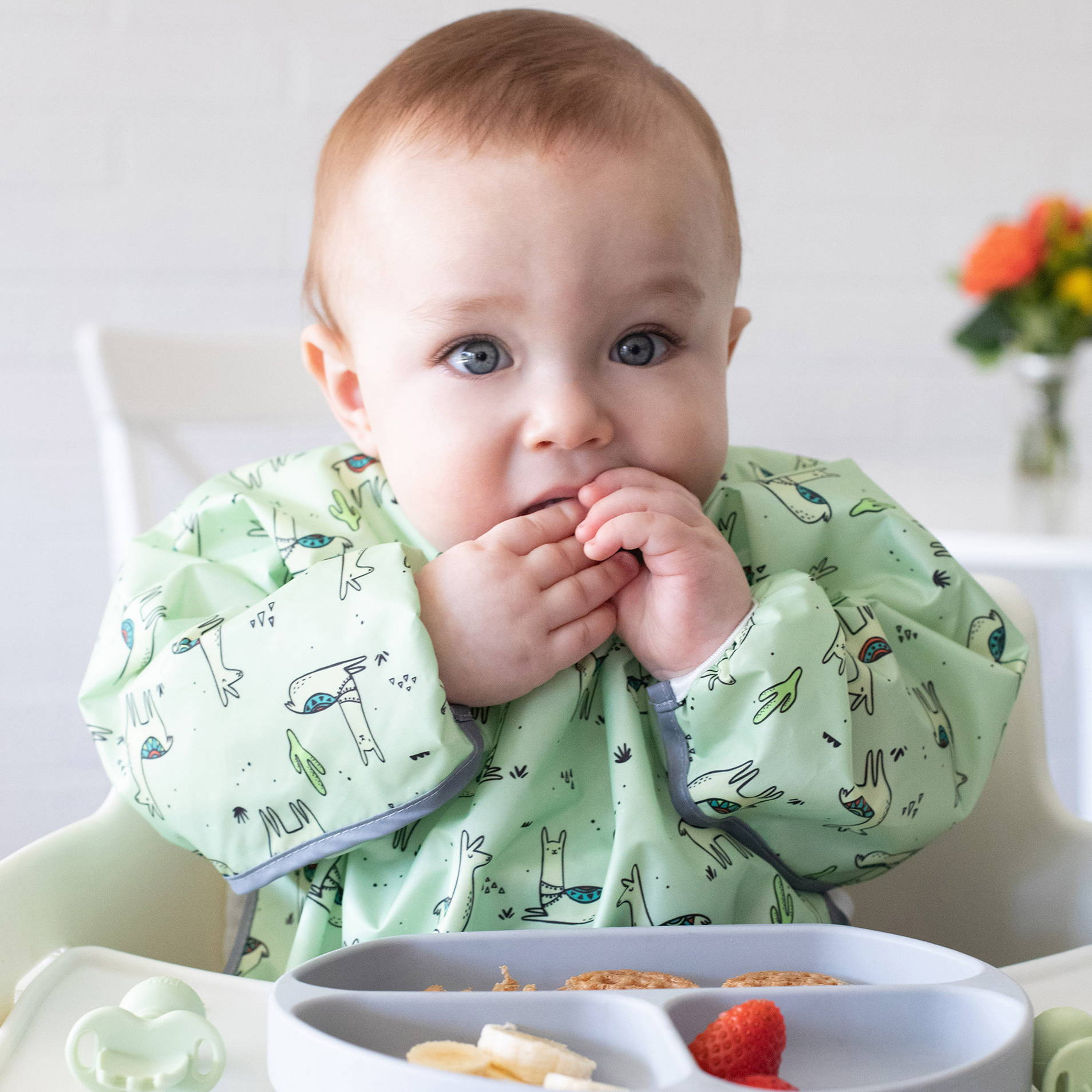 baby eating out of a bumkins silicone grip dish 3-section while wearing a bumkins sleeved bib